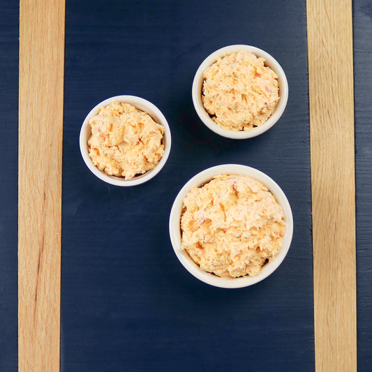 Pimento cheese spread in three bowls on a blue board