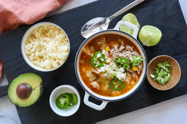 southwest chicken soup in bowl on a board with cheese, limes and avocado