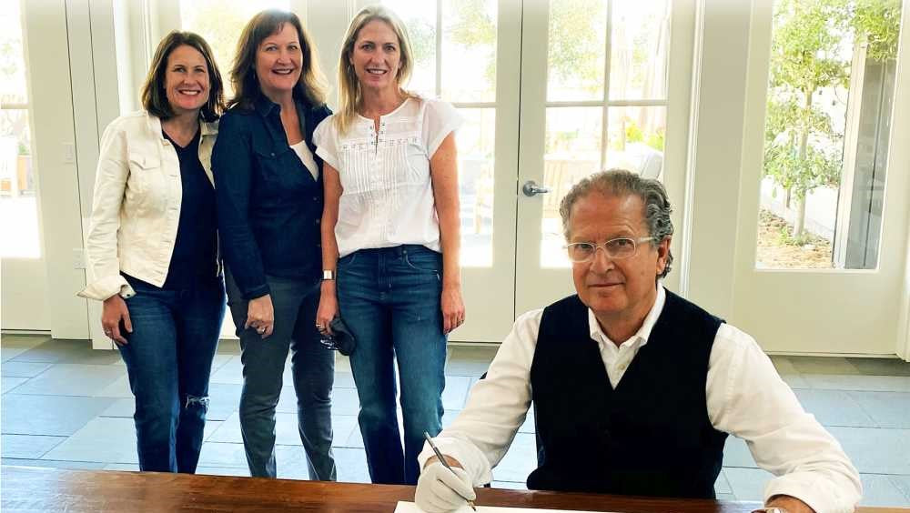 The three owners of Point Reyes Farmstead Cheese standing behind artist, Michael Schwab while he signs artwork commissioned for the 20th anniversary of the company