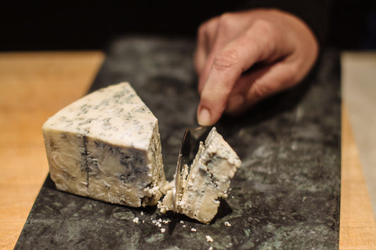 someone cutting a wedge of bay blue cheese