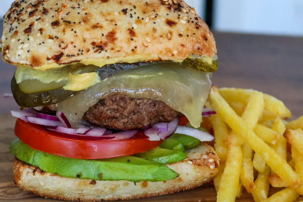 burger with melted toma, pickles, avocado, tomato on a seeded bun