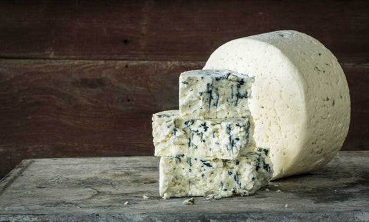 A wheel of Original Blue cheese behind three stacked pieces of Original Blue cheese