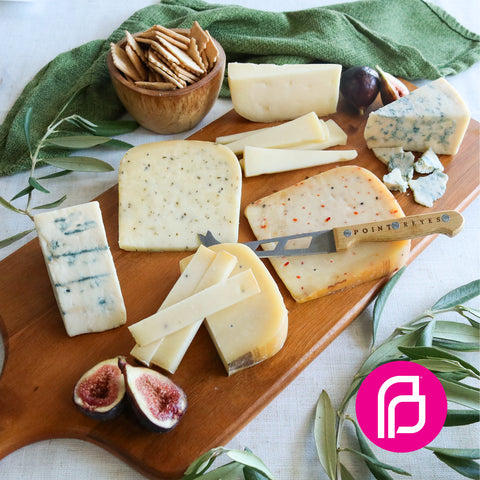 Product: Assorted cheeses on a wooden board with figs, crackers, and a knife.