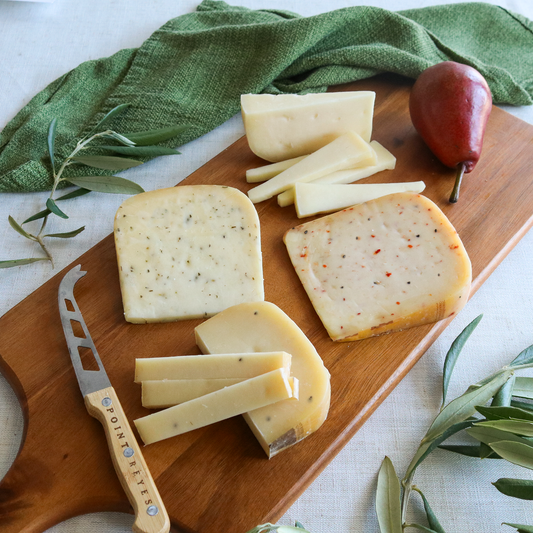 Wooden cutting board with sliced cheese, a knife, and pears on a light background